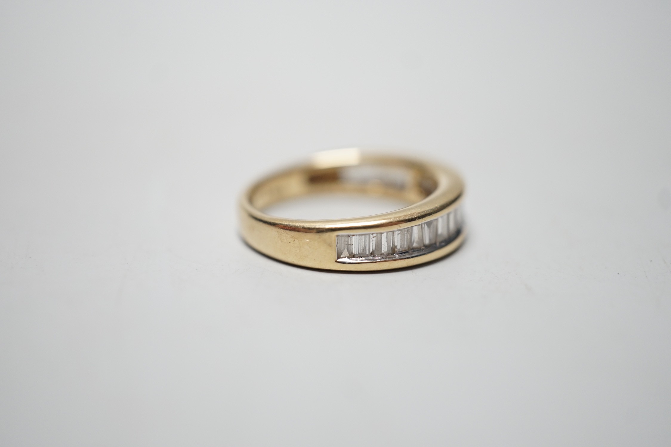 A modern 14k yellow metal and graduated baguette and trapeze cut diamond set half eternity ring, size N, gross weight 4.6 grams.